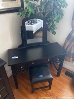 Black wooden desk with attached mirror and small matching chair positioned in room corner