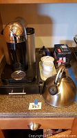 Photo shows Nespresso coffee machine, coffee pod holder, cups and kettle on countertop