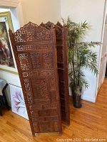 Full view of the wooden carved room divider beside the artificial bamboo plant in decorative vase