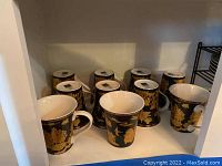 View of the 10 fine china cups with black and gold Forbidden City design in shelf space.