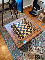 Full view of the wooden chess table with chess set arranged on rug.