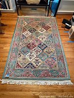 Full view of the rectangular green oriental rug laid on a hardwood floor, showing the full pattern and fringed edges.