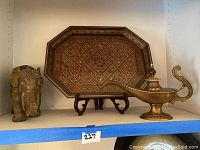 Three decorative Indian style items displayed on a shelf: carved elephant figurine, brass oil lamp, and decorative tray on stand
