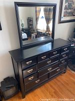 Front view of black credenza with multiple drawers, silver drop handles, and attached mirror reflecting room interior.