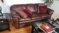 Full view of the brown leather Lazyboy couch with four pillows, placed in a living room setting with hardwood floor.
