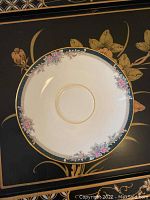 Close-up of a saucer showing the floral pattern and teal border with gold trim.