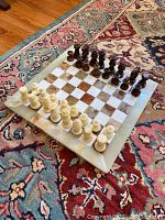 Full view of the marble chess board with all chess pieces arranged in starting positions on a patterned rug.