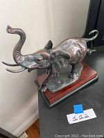 Photo of the running elephant sculpture from a side angle showing detailed anatomy, trunk raised, and wood base.