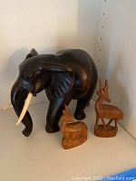 Front view of large black elephant figurine with two smaller wooden antelopes, all hand-carved with natural textures.