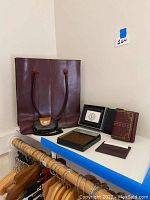 Five wallets of different brands displayed alongside two small cases and one red carrying bag on a white surface.