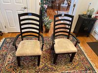 Two wooden captain chairs with beige cushioned seats on a patterned rug near a doorway.
