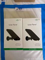 Full frontal image of two unopened Arlo Solar Panel charger boxes, showing product image and branding on front.