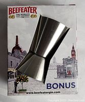 Front and side views of the Beefeater branded stainless steel jigger shot glass with original packaging featuring London landmarks and promotional text.