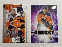 Two Connor McDavid hockey cards displayed side by side, one showing McDavid in blue and orange uniform with electric background and the other showing him sitting in the Oilers locker room surrounded by gear.
