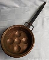 Side view of copper pan showing six indentations and cast iron handle with loop