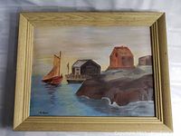 Framed oil painting of a sailboat near a dock with wooden buildings on rocky shore, signed by artist K. Ryans.