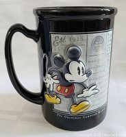 Side view showing black ceramic mug with colorful Mickey Mouse image and text