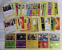 Top view of an assortment of Pokemon cards laid out, showing a mix of energy cards, Pokemon character cards including holographic ones, and various trainer cards.