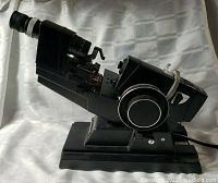 Side angle view of the complete Topcon LM-6E lensmeter showing eyepiece, focusing wheel, and base with power connection.