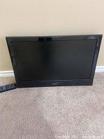 Black 24 inch Insignia flat screen TV with remote control placed on carpet against beige wall