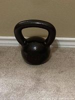 Black cast iron kettlebell weighing 35 pounds on carpeted floor next to white baseboard.