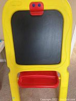 Yellow framed Crayola chalkboard easel with black writing surface and red tray showing crack on marker holder tray