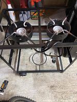 Top view photo of a double outdoor propane burner on a black metal frame. Shows two circular burners with propane hose and regulator attached.