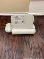 White Swingline electric hole punch with paper guide and power switch, placed on a wooden floor.