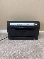 Front view of FoodSaver black vacuum sealer machine placed on carpet against wall.