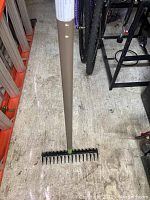 Top view showing full rake with brown handle and black metal tines on the concrete floor surrounded by other tools.