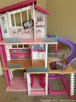 Front angled view showing facade, three levels, interior wallpaper details, balcony, and purple slide.