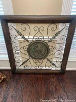 Front view of large square metal wall art with ornate central medallion and decorative leafy metal design within dark wooden frame