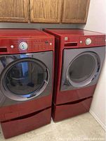 Front and side view of red Kenmore Elite dryer next to matching washer showing exterior finish and pedestal.