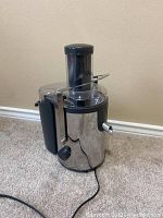 Front-side view of the stainless steel juicer showing feed chute, juice spout, and power cord