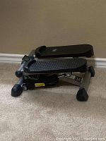 Front side view of compact stair stepper exercise machine with black textured foot pedals and digital display screen