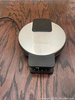 Top view of Cuisinart waffle maker with stainless steel lid, black handle, and browning level dial.