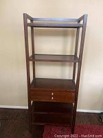 Full frontal view of the brown wooden shelf with drawer and multiple shelves against a beige wall.