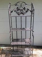 Full front view of the metal folding bakers rack showing all four shelves and decorative leaf detail on back panel.
