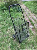 Side view of black folding steel rolling laundry basket shopping cart on a grass path