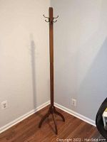 Full view of the freestanding coat stand showing its height, base, and overall shape against a wall.