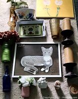 Various decorative vases, planters, framed paintings including white flowers and cat images, blue bottle, flower pots and trays arranged on floor.