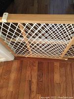 Natural wood framed baby or pet gate installed in a doorway with white mesh center and locking mechanism visible.