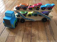 Front view of wooden toy tractor and trailer with 6 race cars loaded, showing colors and design details.