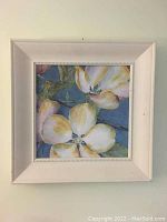 Front view of framed flower painting showing three large white and yellow flowers with green leaves on blue-gray background.