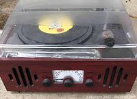 Front view of vintage style FM/AM radio and record player with wooden case and clear plastic cover showing turntable and control panel with tuning dial.