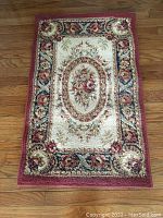 Full view of small Shaw Rugs area rug, rectangular with a central oval floral design and aubusson red border on wood floor.