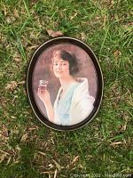 Oval Coca Cola metal tray featuring a vintage woman holding a glass of Coke, placed on grass background showing size and condition.