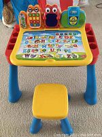 Front view of VTech activity desk with alphabet learning page on desktop and yellow stool in front.