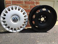 One of the black steel wheels next to corresponding Volkswagen silver plastic hubcap with VW logo