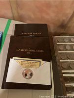 Two brown hardcover albums titled Canadian Small Cents 1920- and Canadian Nickels 1922- with plastic sleeves visible and commemorative coin in envelope